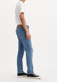 Světle modré džíny z denimu s rovným střihem, s ko ženou nášivkou na zádech a opotřebovanou texturou. Kombinovány s jednoduchým bílým tričkem a černými teniskami.