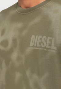 Λαδί βαμβακερό μπλουζάκι με διακριτικό μοτίβο καμουφλάζ, στρογγυλή λαιμόκοψη και ελαφρώς γκρι λογότυπο "DIESEL" τυπωμένο στο στήθος.