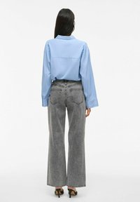 Camisa de manga larga azul claro combinada con pantalones de pinzas grises de cintura alta y pierna ancha, y zapatos de tacón negro. Suela de goma visible.
