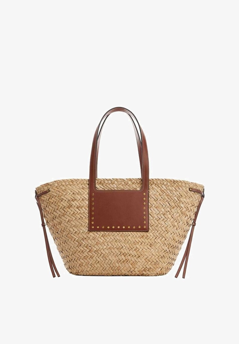 Sac fourre-tout en paille tissée avec des anses en cuir marron, un patch carré en cuir avec des clous en laiton, et des pampilles latérales en cuir.