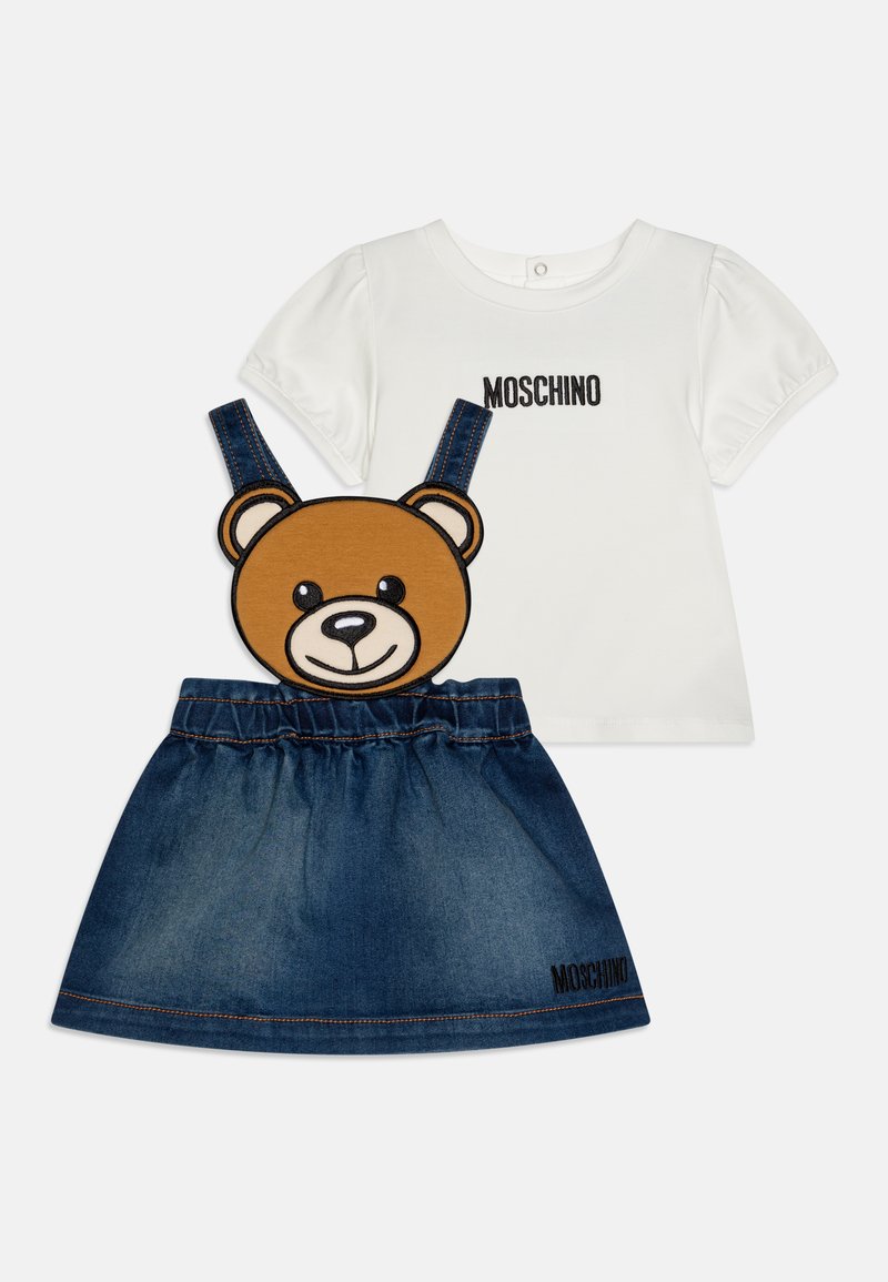 Balta T-krekls ar puff piedurknēm un melnu "Moschino" tekstu, kopā ar džinsu svārkiem, kuriem ir lāča seja uz siksnām un elastīga josta.