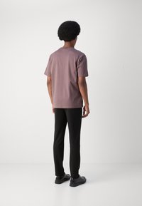 Tricou din bumbac lavandă cu mânecă scurtă, asortat cu pantaloni negri slim-fit și pantofi negri, văzut din spate. Textură netedă, design minimal.