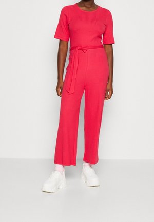 Fuchsia geribde jumpsuit met korte mouwen, strik taille, wijde benen, gestructureerde stof en gecombineerd met witte chunky sneakers.