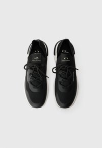 Pantofi sport negri cu o parte superioară texturată, guler elastic și accente albe. Prezintă șireturi și o talpă de culoare deschisă.