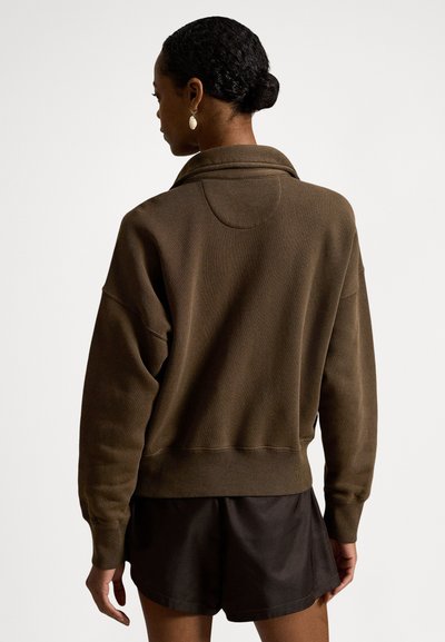 Brun, oversized genser med fold-over krage, ribbestrikkede mansjetter og kant. Brukt med mørke shorts, teksturert stoff med et avslappet design.