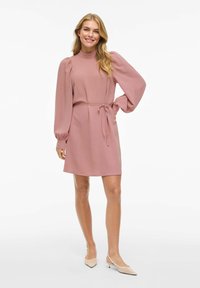 Kortärmad rosa klänning med texturerat tyg, hög krage och åtsittande midja, med utsvängda ärmar och ett knytband.