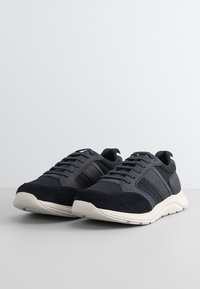 Sneakers da uomo in blu navy scuro, realizzati in una combinazione di materiali in rete e suede, con suola in gomma bianca testurizzata e lacci piatti.