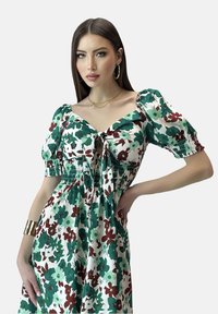 Blumenmusterkleid in Grün, Kastanienbraun und Weiß, mit kurzen Puffärmeln und einem Bindegürtel-Detail. Aus leichtem Stoff gefertigt.