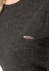 T-paita tummanharmaata puuvillaa, jossa on pyörteilevä kuvio. Rinnassa metallinen logotagi. Pehmeä rakenne, crew-neck -kaulus.