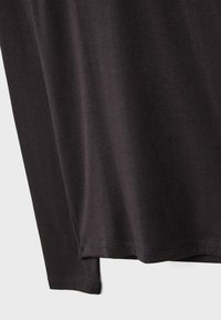 Czarna bawełniana koszula z długim rękawem o gładkiej fakturze. Posiada zaokrąglony dekolt i lekko wydłużony tylny dół. Prosty i nieozdobiony design.