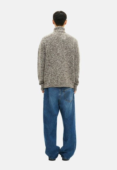 Pullover chunky a maglia con texture in tonalità beige e marrone, abbinato a jeans in denim blu medio a vestibilità ampia con dettagli della tasca posteriore.
