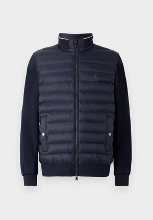 Chaqueta con cremallera en azul marino, con frontal acolchado, mangas lisas, cuello alzado con franjas rojas y blancas, y dos bolsillos con botón a presión.