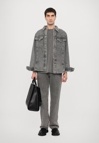 Gray denim jacket with two chest pockets, paired with matching gray pants. A black tote bag in hand, black shoes complete the look.