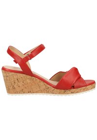 Sandale compensée en cuir rouge avec une semelle en matériaux ressemblant à du liège, présentant un design de brides croisées et une sangle de cheville ajustable. Semelle texturée pour une meilleure adhérence.