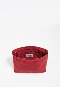 Bolso de mano de nylon rojo con un acabado texturizado, que cuenta con un interior espacioso, bolsillos laterales y un cierre con cremallera. Etiquetado en el interior con el nombre de la marca.