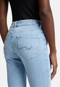Jeans in denim azzurro chiaro con vita alta, gamba dritta e due tasche posteriori con cuciture a motivo onda. Etichetta visibile alla vita.