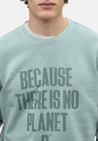 Sudadera verde claro con cuello redondo, con texto gris en negrita que dice "PORQUE NO HAY UN PLANETA B." Tejido suave y texturizado.