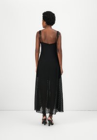 Black maxi dress with spaghetti straps, textured mesh fabric, and a flowing silhouette. Features a dotted pattern and a low back design.