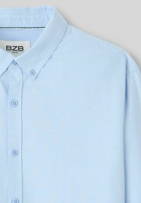 Chemise col bleu clair avec fermeture à boutons, manches longues et détails de texture subtils. L'étiquette indique "BZR COMFORT."