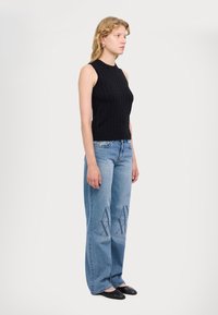 Top senza maniche a maglia nera con motivo testurizzato, abbinato a jeans palazzo blu chiaro con logo sbiadito sulla parte anteriore e ballerine nere.