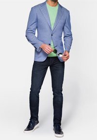 Světlomodrý blazer, zelené tričko, tmavé džíny a námořnické tenisky. Blazer má klopový límec, dvě knoflíky a tři přední kapsy.