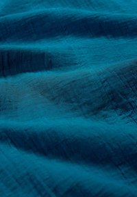 Gros plan sur un tissu bleu texturé avec des coutures visibles et des plis doux créant des variations de lumière et d'ombre.