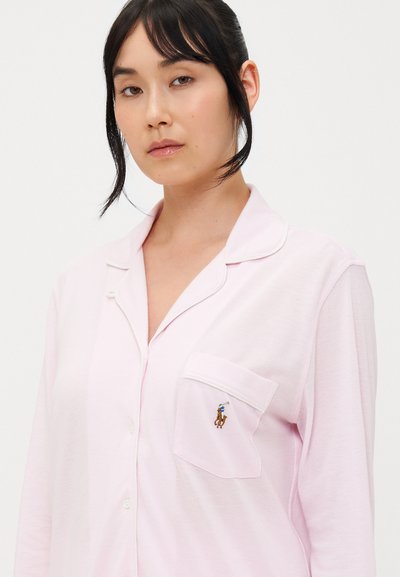 Ροζ πιτζάμα με κολάρο, κουμπιά μπροστά και τσέπη με κεντημένο λογότυπο. Μαλακό ύφασμα με απαλό υφή.