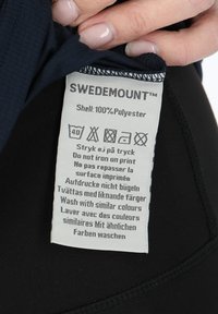 Tessuto in poliestere blu navy con un'etichetta di cura che mostra le istruzioni per il lavaggio in più lingue, cucita con filo nero lungo il bordo.