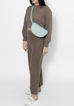 Donna che indossa un completo marrone in maglia a due pezzi con felpa corta, pantaloni a gamba larga, mocassini bianchi senza lacci e una borsa a tracolla azzurro chiaro.