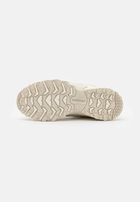 Suola di sneaker con scanalature profonde, prevalentemente beige chiaro, caratterizzata da una superficie testurizzata e motivi rialzati prominenti per una migliore aderenza.