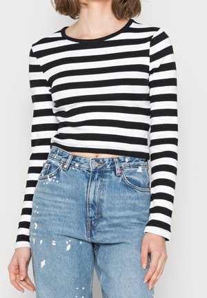 Stribet sort og hvid langærmet cropped top, ribbet stof, rund halsudskæring, parret med lyseblå slidte denim jeans med malingstænk.