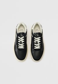 Svart lær sneakers med hvite detaljer og lacéer, med en teksturert overdel og en kremfarget gummisåle. Logo synlig på tungen.