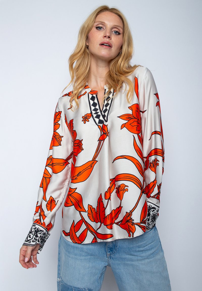 Bluzka z długim rękawem z lekkiego satenu, w żywych pomarańczowych wzorach kwiatowych na białym tle. Czarne haftowane akcenty przy dekolcie i mankietach.