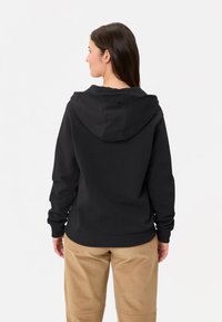 Felpa nera con cappuccio a coulisse, polsini e orlo a costina. Presenta un logo sul retro ed è caratterizzata da una vestibilità rilassata. Indossata con pantaloni color khaki.