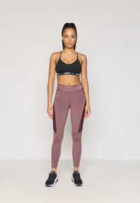 Soutien-gorge de sport noir avec une bande de marque ; leggings bordeaux avec des panneaux latéraux texturés ; assortis avec des chaussures de sport noires.