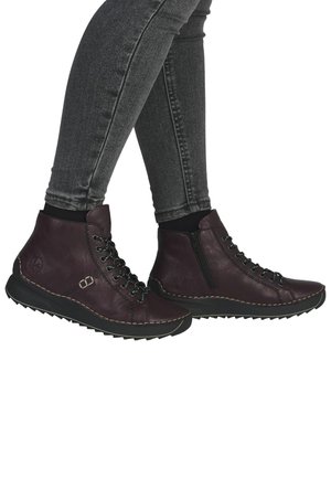 Bottes chelsea violettes en cuir, avec une fermeture éclair et un laçage sur le devant, des surpiqûres et une semelle en caoutchouc noir texturé.