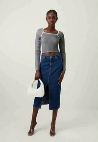 Szürke bordázott, hosszú ujjú crop top, magas derekú farmer szoknya elülső hasítékkal, átlátszó sarkú szandál és fehér, texturált kézitáska.