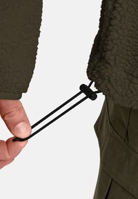 Fleece jacket in dark olive with textured exterior. Black drawstring pulled by hand for adjustment, featuring a plastic toggle.