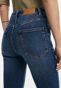 Högmidjade mörkblå jeans i denim, med en läderlapp på midjan och kontrasterande sömmar på bakfickorna.
