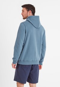 Hooded sweatshirt in soft blue fabric, featuring a kangaroo pocket, ribbed cuffs, and hem. Worn with dark shorts, shown from the back.