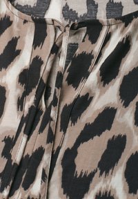Gros plan sur un tissu imprimé léopard beige et noir avec une encolure en forme de trou de serrure et une fermeture par lien en tissu.