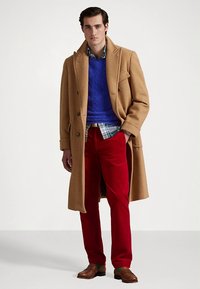 Παλτό από μαλλί καμήλας, μπλε πουλόβερ με πλέξη κοτσίδα, πουκάμισο καρό, κόκκινο παντελόνι, καφέ δερμάτινα παπούτσια. Εντυπωσιακές υφές και αντιθετικά χρώματα.