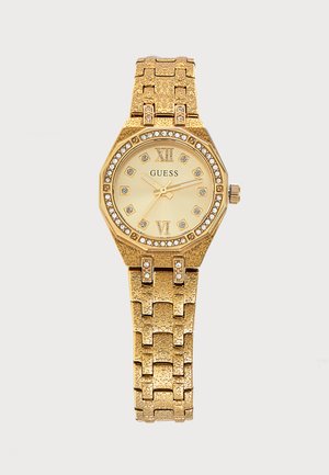 Χρυσού χρώματος ρολόι χειρός Guess με σημεία ώρας από κρύσταλλα, ρωμαϊκούς αριθμούς στις 12 και 6, και υφασμένη μεταλλική σύνδεση.
