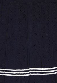 Neuleme navy-coloured mekko, jossa on teksturoitu kuvio zigzag-muotoiluilla ja pieniä aukkoja. Mekkoa korostaa valkoinen raidallinen nauha helmassa.