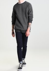 Ciemnoszara bluza crewneck z raglanowymi rękawami, w zestawie z dopasowanymi ciemnymi dżinsami i czarnymi sneakersami z białymi akcentami.