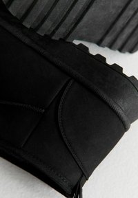 Primo piano della tomaia in suede nero e della suola spessa in gomma di un robusto stivale da esterno.