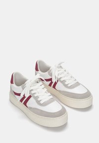 Weiße und graue Sneaker mit roten Akzenten, aus strukturiertem Leder und Wildleder, mit flachen Schnürsenkeln und einer dicken, strukturierten Gummisohle.