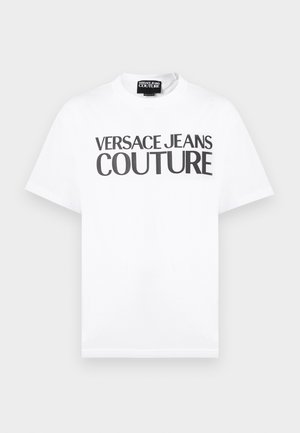 Valge lühikeste varrukatega T-särk, millel on rinnal must tekst "VERSACE JEANS COUTURE" ja väikese brändisildiga kaeluse sees.