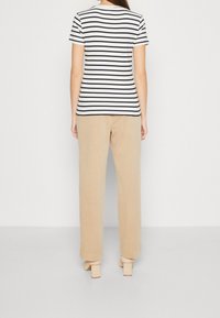T-shirt à manches courtes rayé en blanc et marine, associé à un pantalon beige clair. Le pantalon a une coupe décontractée avec des ourlets retroussés. Escarpins unis.