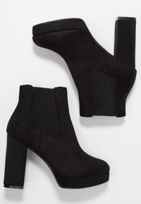 Botines negros con un exterior de ante, paneles laterales elásticos, plataforma alta y tacones gruesos para mayor altura y estabilidad.